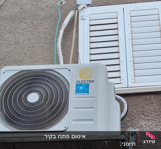 יחידת מיזוג אוויר מותקנת על קיר חיצוני ליד תריסים